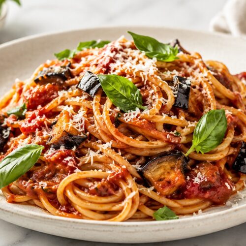 Spaghetti alla Norma mit Auberginen, Tomatensauce und Basilikum auf einem hellen Teller